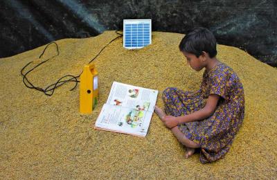 A young girl in India studies on top of a pile of harvested rice by the light of a solar-powered lamp.