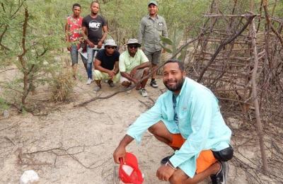 Implementers of a habitat conservation effort pose for a photo in a dry landscape surrounded by small saplings