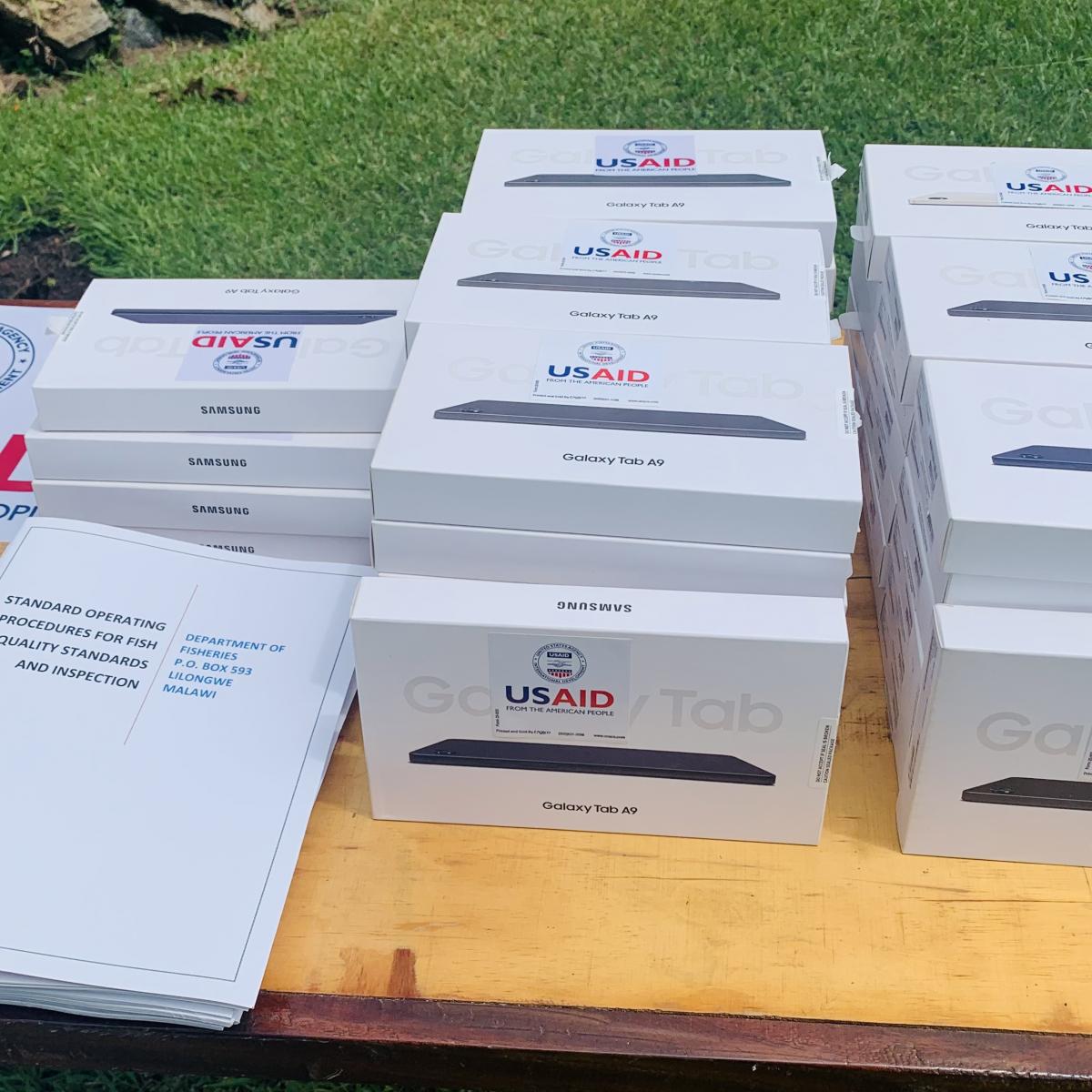 A pile of USAID-branded smart tablets and their user manuals on a table.