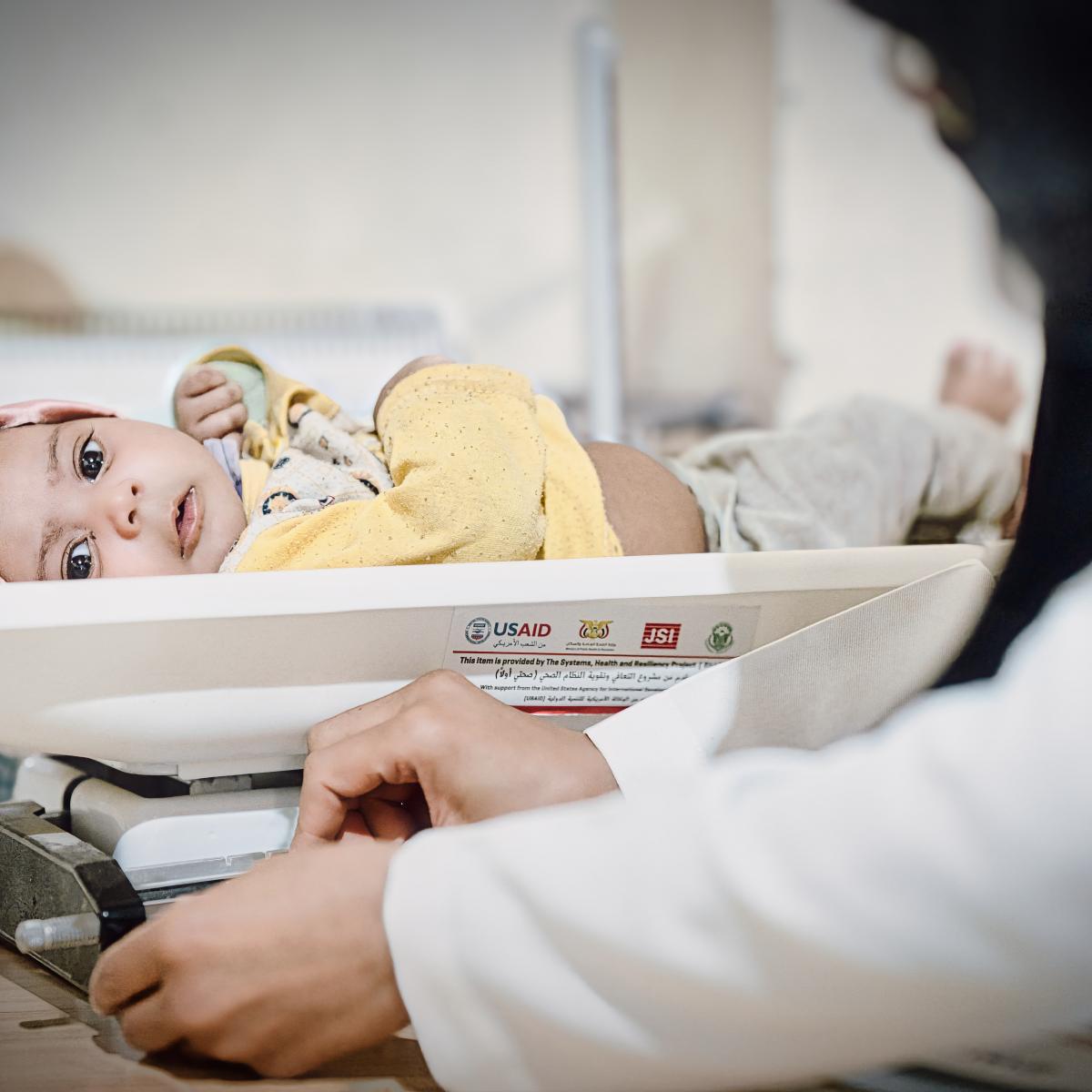 A USAID-supported midwife weighs a baby on equipment provided by USAID. 