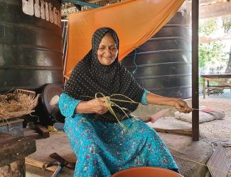 A woman makes a coconut stick broom at Fuvahmulah Atoll Biosphere Reserve, Maldives. 