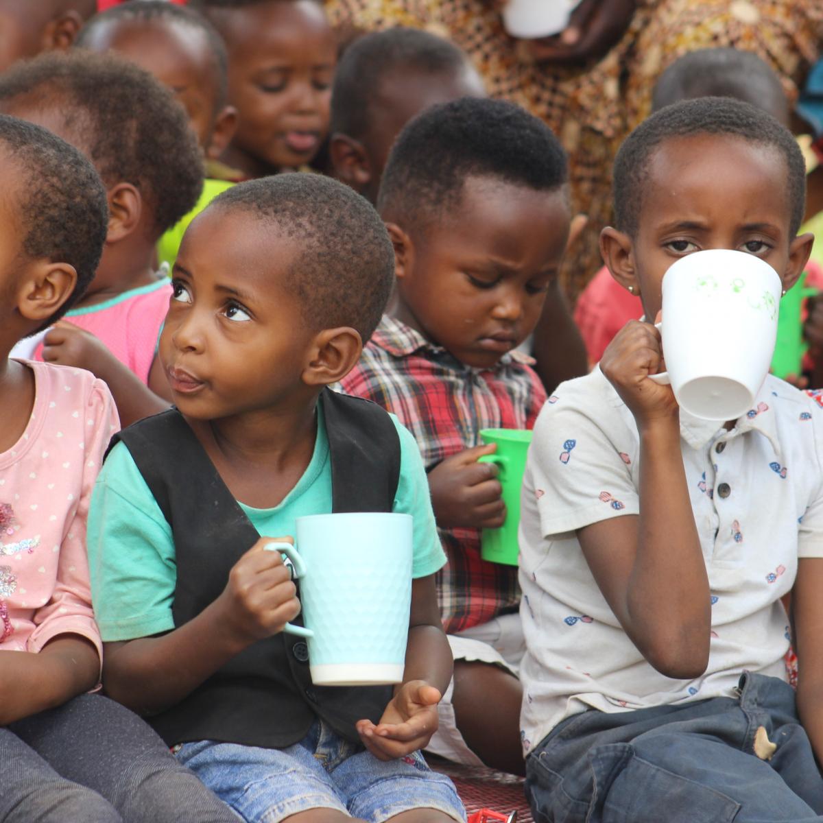 Children drinking milk while seated on the floor of an early childhood development center in Rwanda