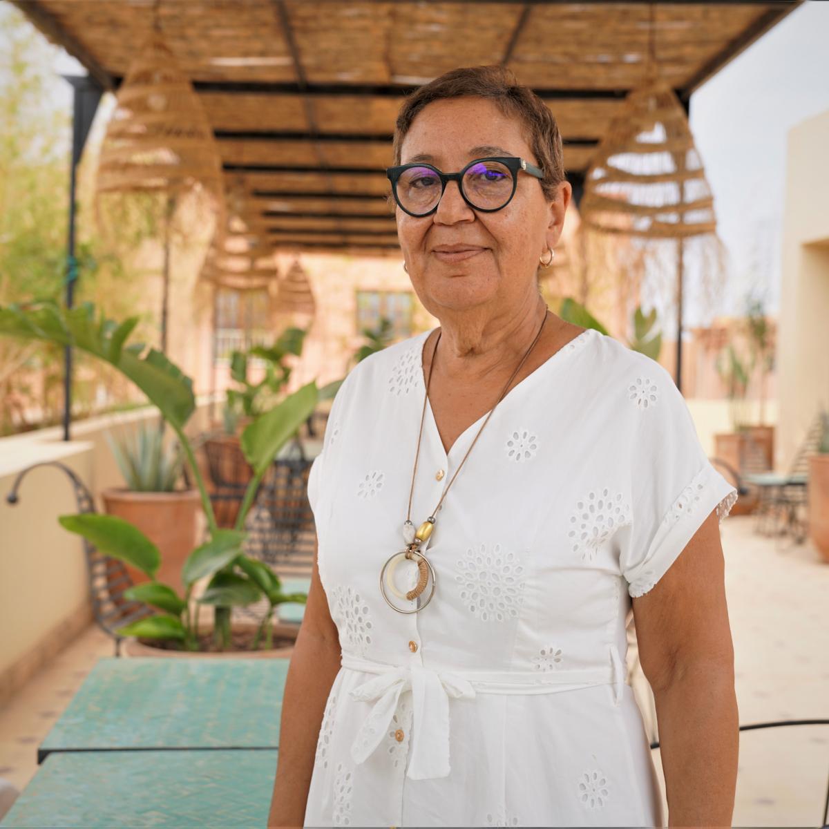 A Moroccan woman smiles and proudly stands in a rooftop restaurant looking at the camera.