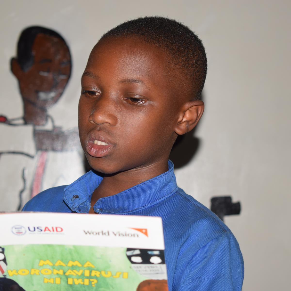 Sarah reading a book printed with the support of USAID.