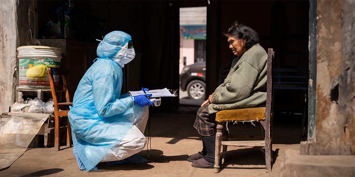 Medic wearing a protective suit interviewing an elder woman 