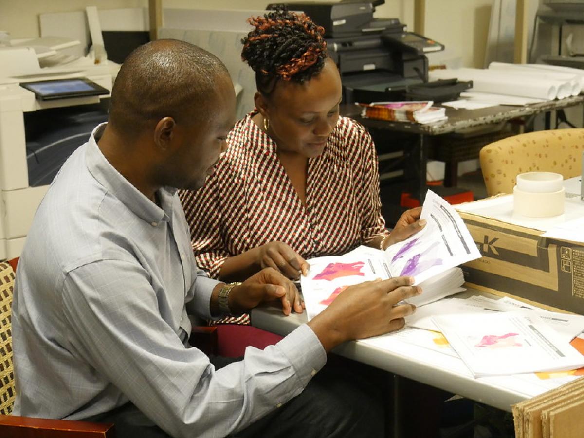 Photo of two people sitting at a desk and looking at a printed map (Photo Credit: USAID)