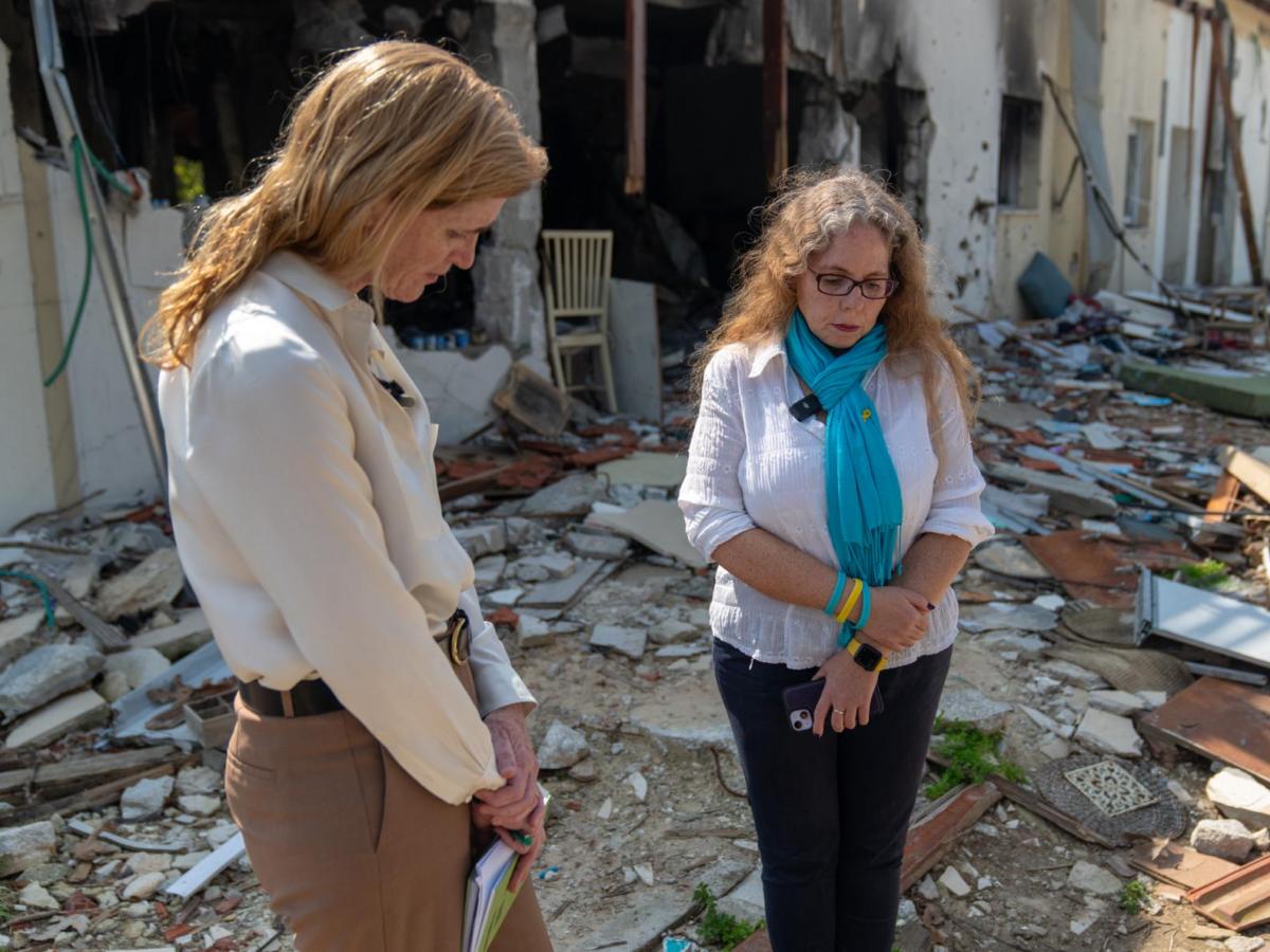 Two women standing side by side in a moment of silence surrounded by the rubble and remains.