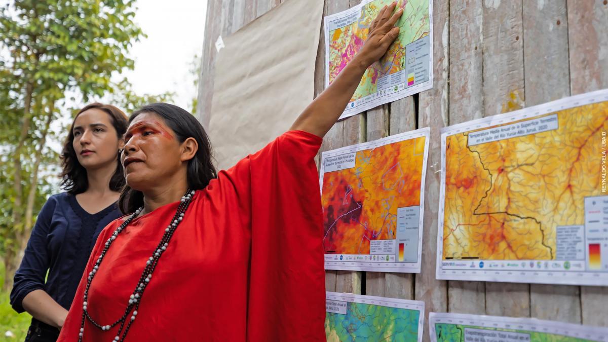 A woman points to satellite images hanging on a wall