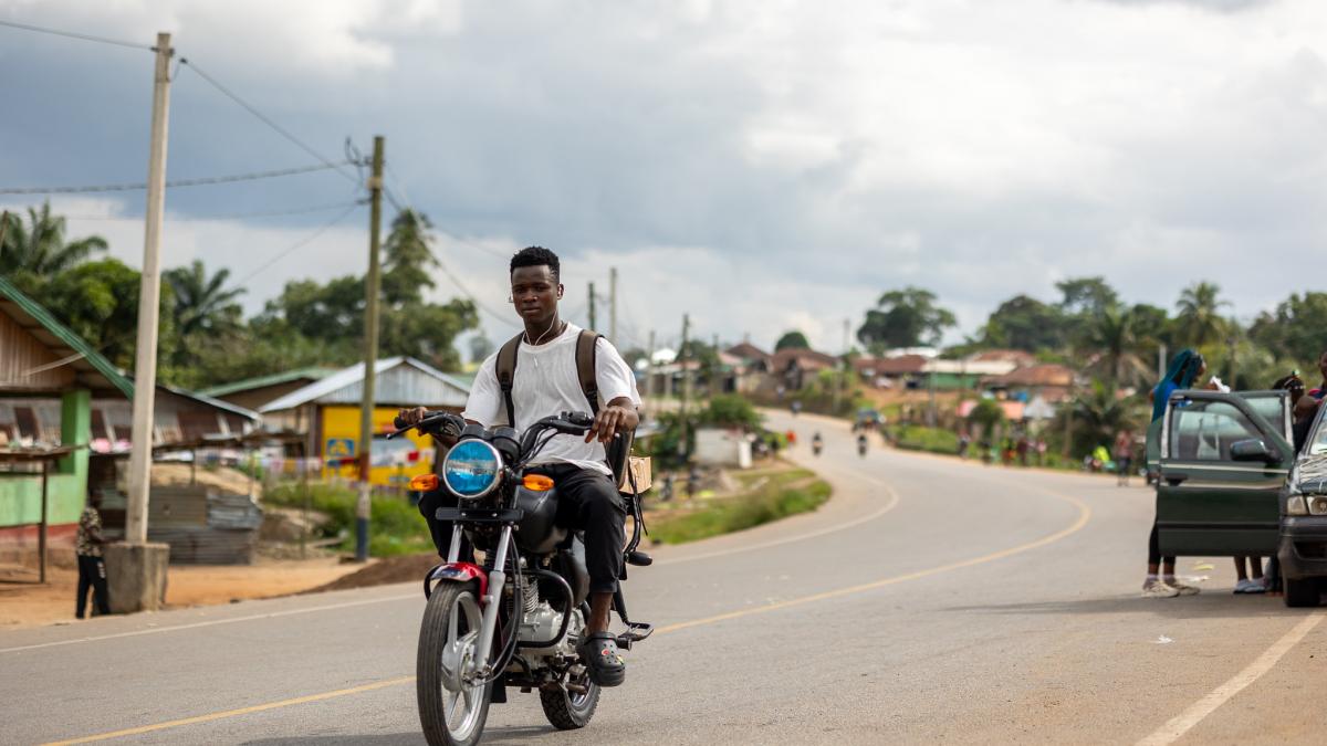 An African man riding a motorbike with transmission lines behind him.