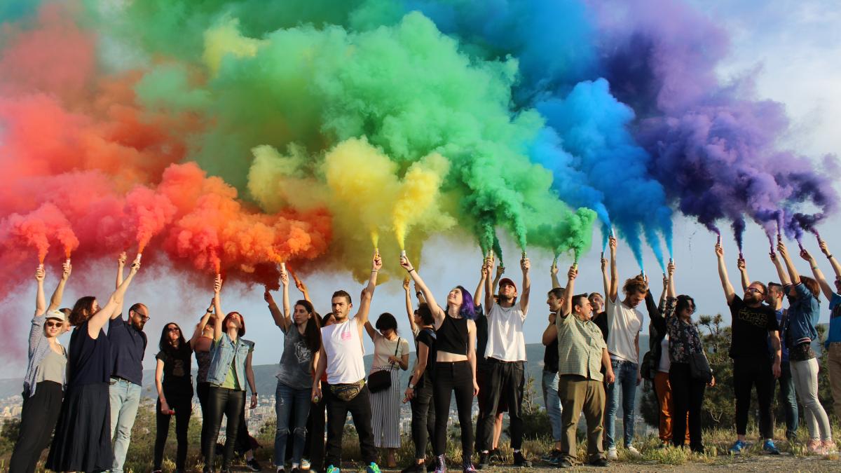 A group of people in a field release a rainbow sequence of powder into the air. 