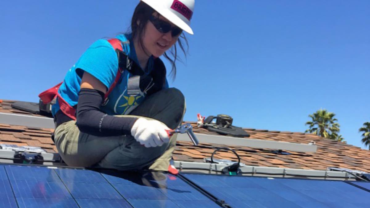 A female Filipino solar engineer installs a photovoltaic array on a rooftop.