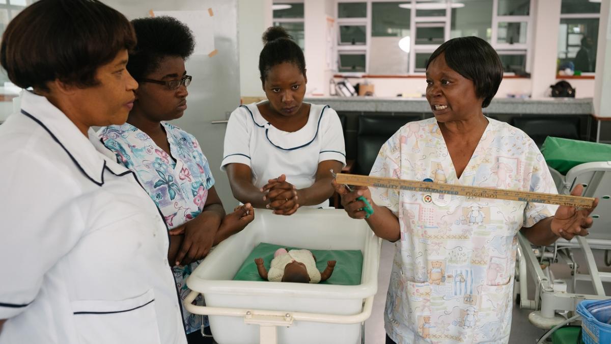 A group of women stand near an infant in a hospital cradle.