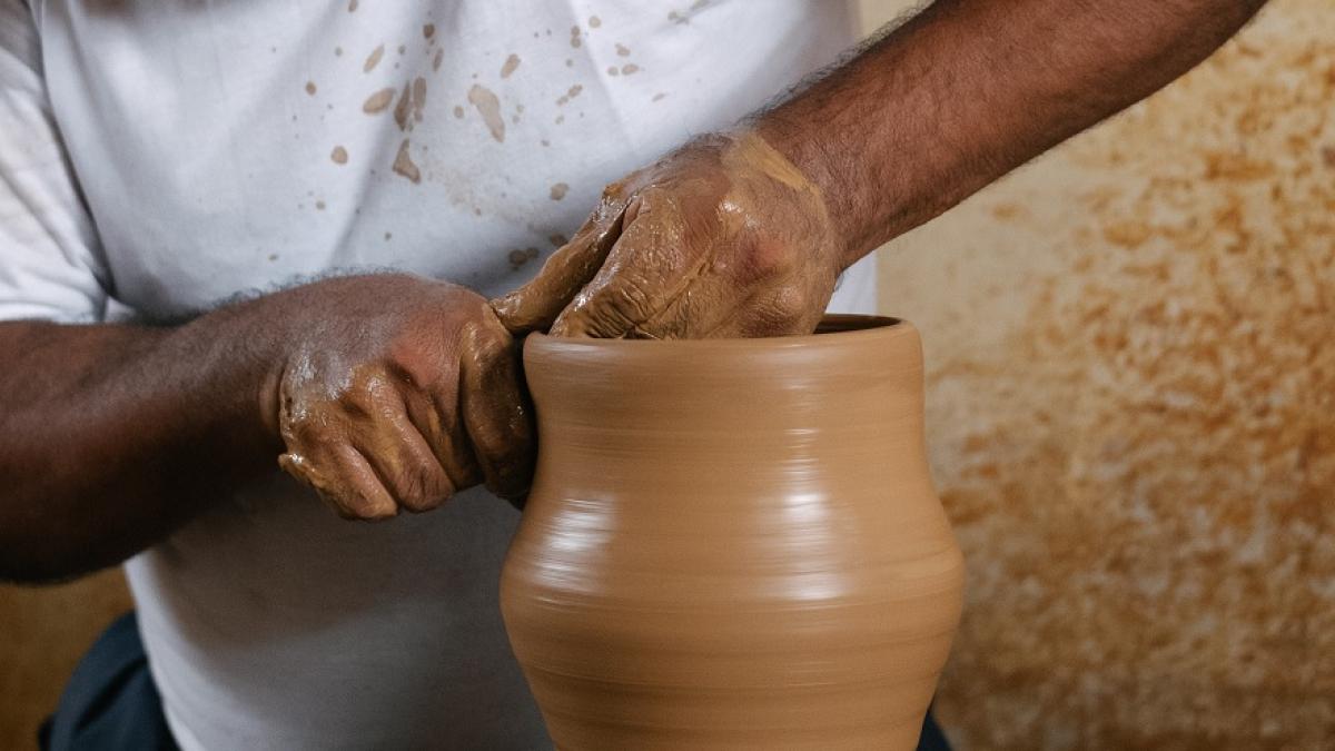 Hands work on a ceramic pot on a pottery wheel.