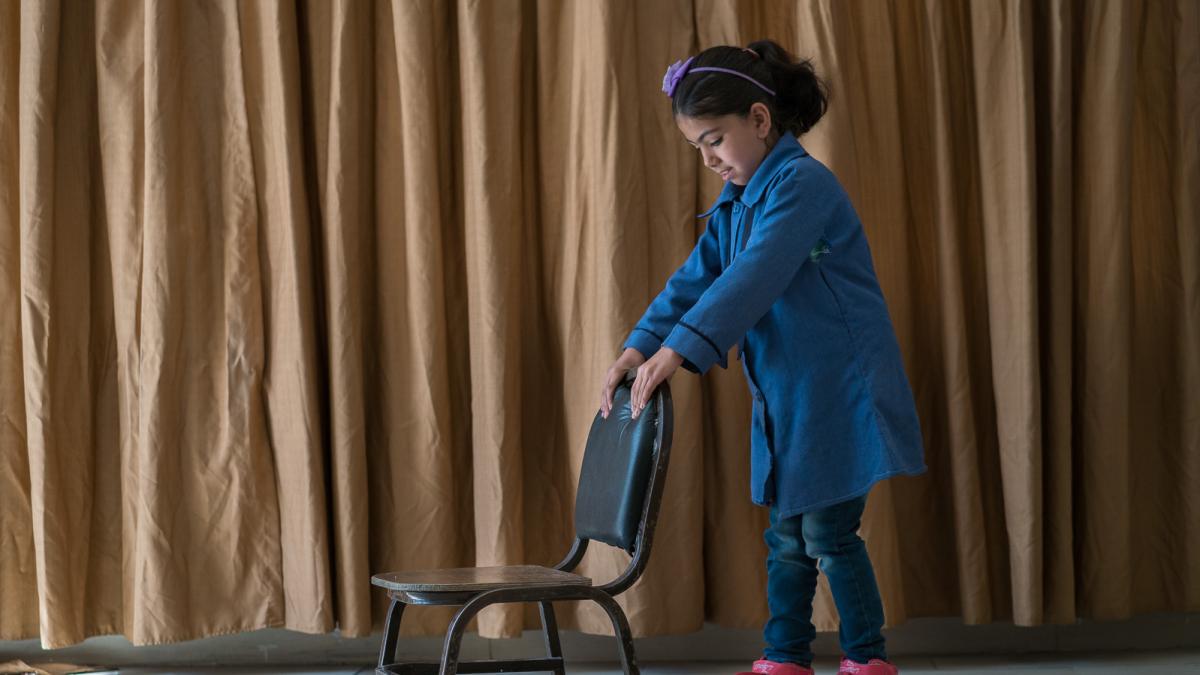 A girl stands behind a chair.