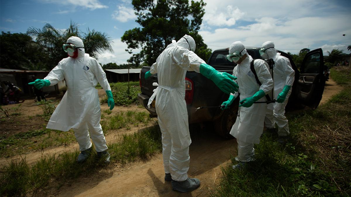 Health workers in hazmat suits standing next to a truck