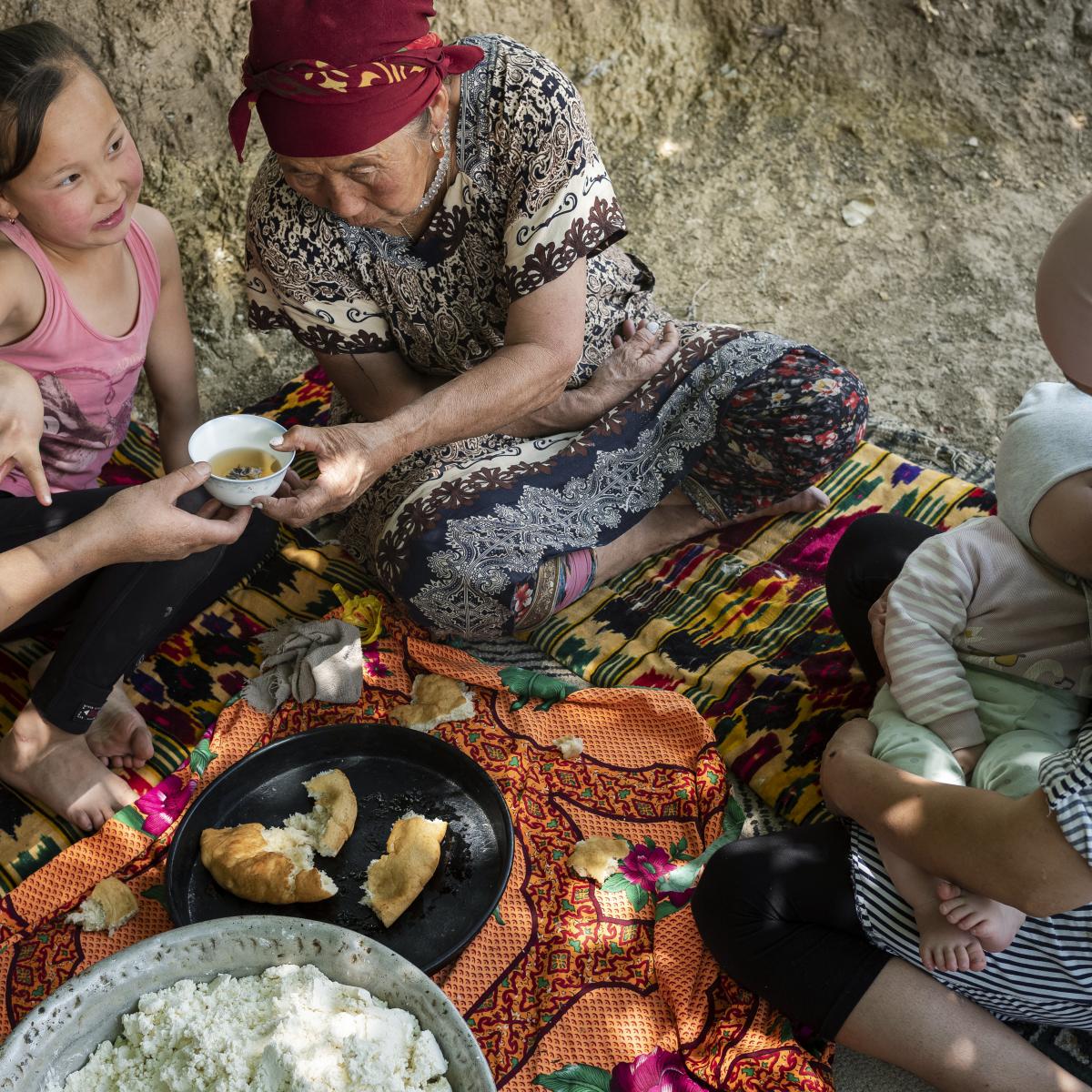 two women and two children sitting on a blanket and eating a meal