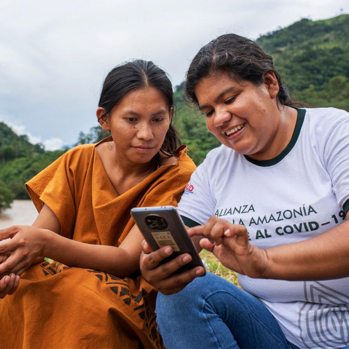 One of the project's professionals teaching an indigenous young woman how to use an app on a cellphone in the Amazon rainforest