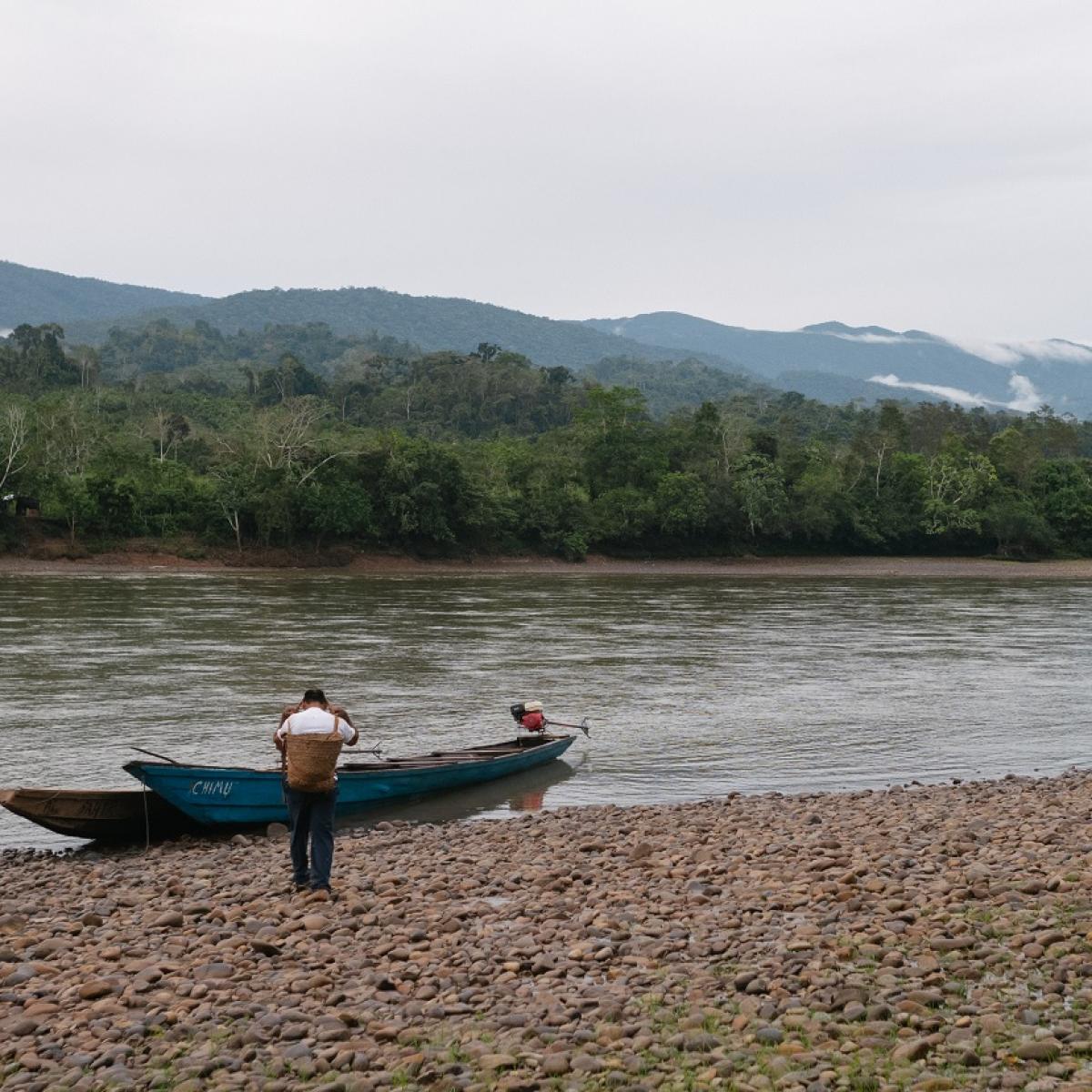 A man walks along a rocky river bank, approaching a small skiff boat.