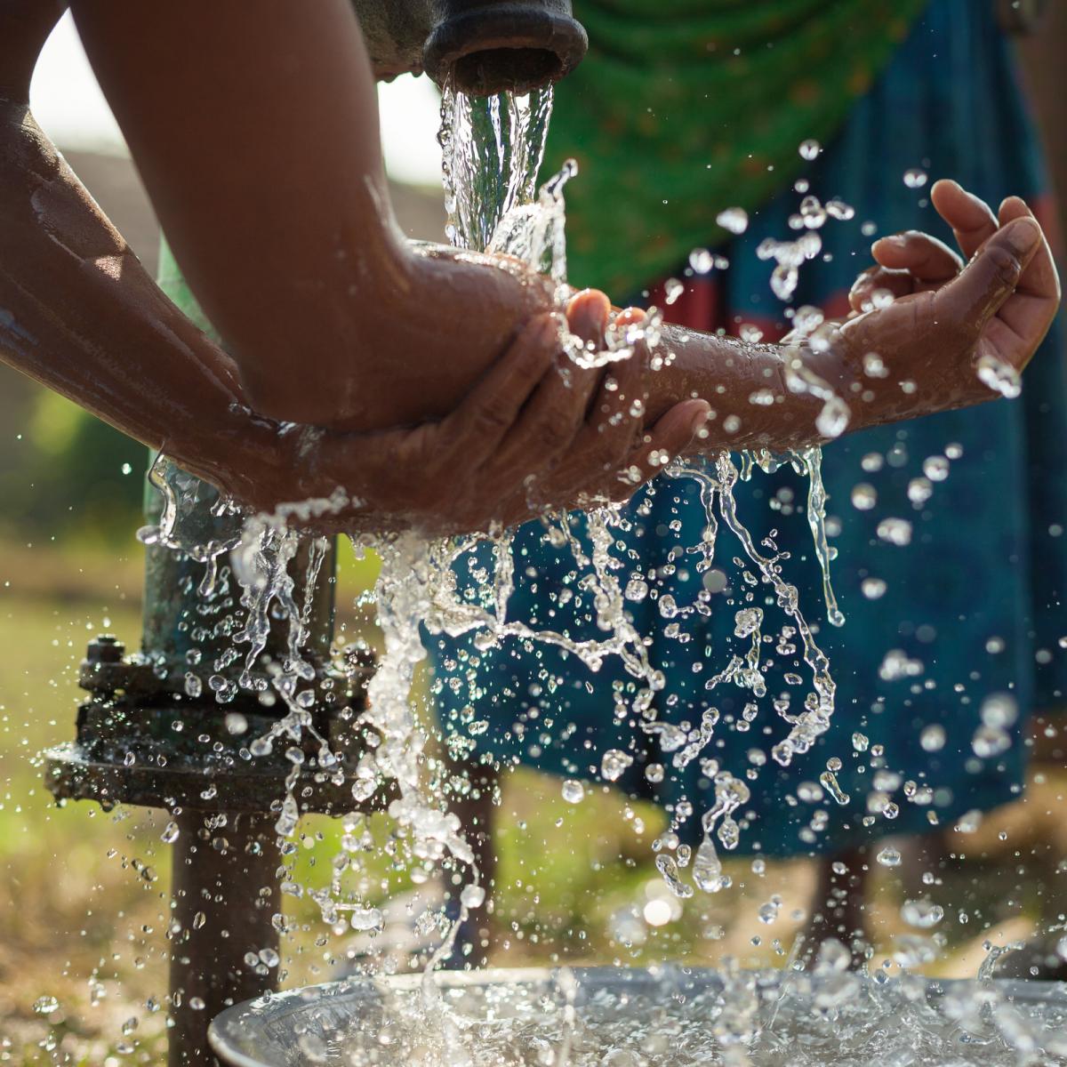 Hands being washed at an outdoor faucet.
