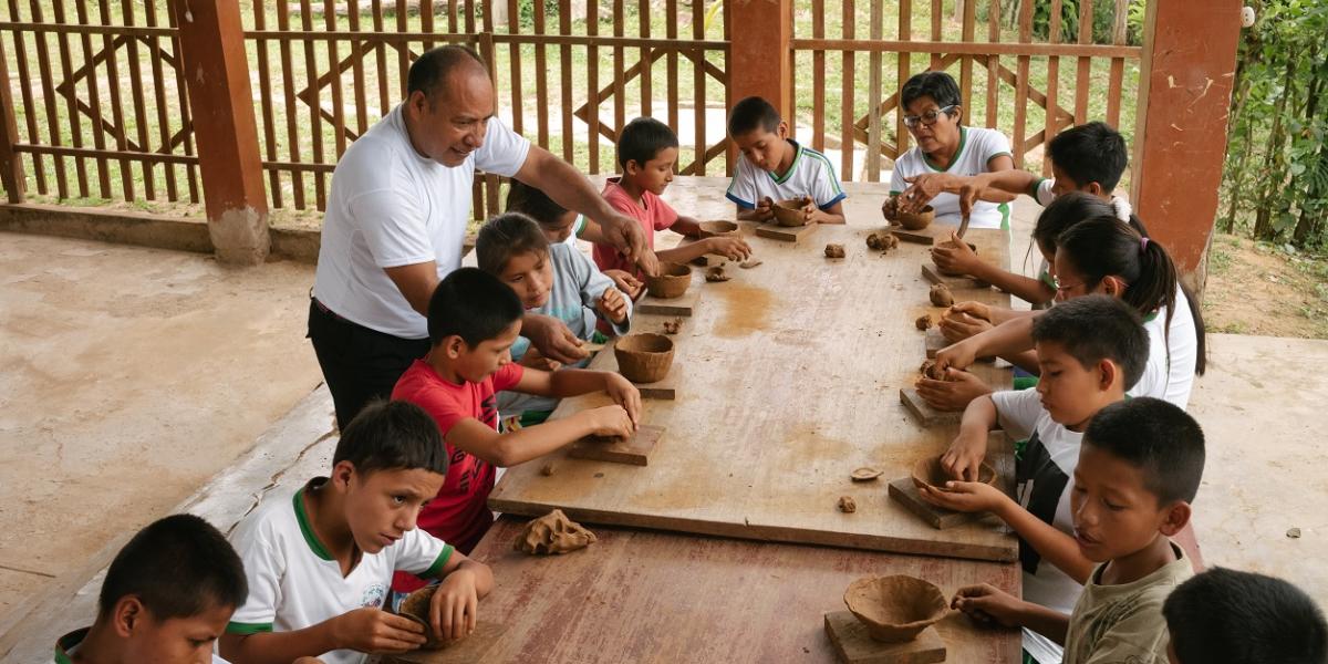 Students make clay pots at an outdoor table.