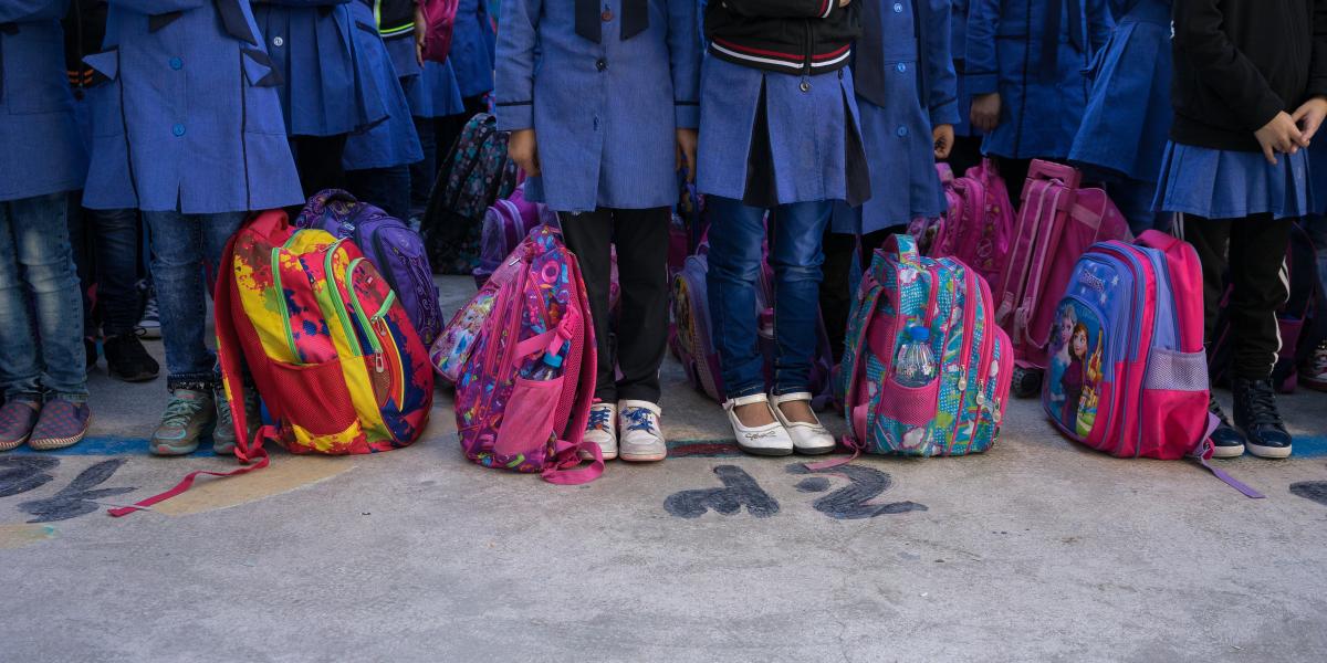 Girls in school uniforms shown from the waist down and including their colorful backpacks.