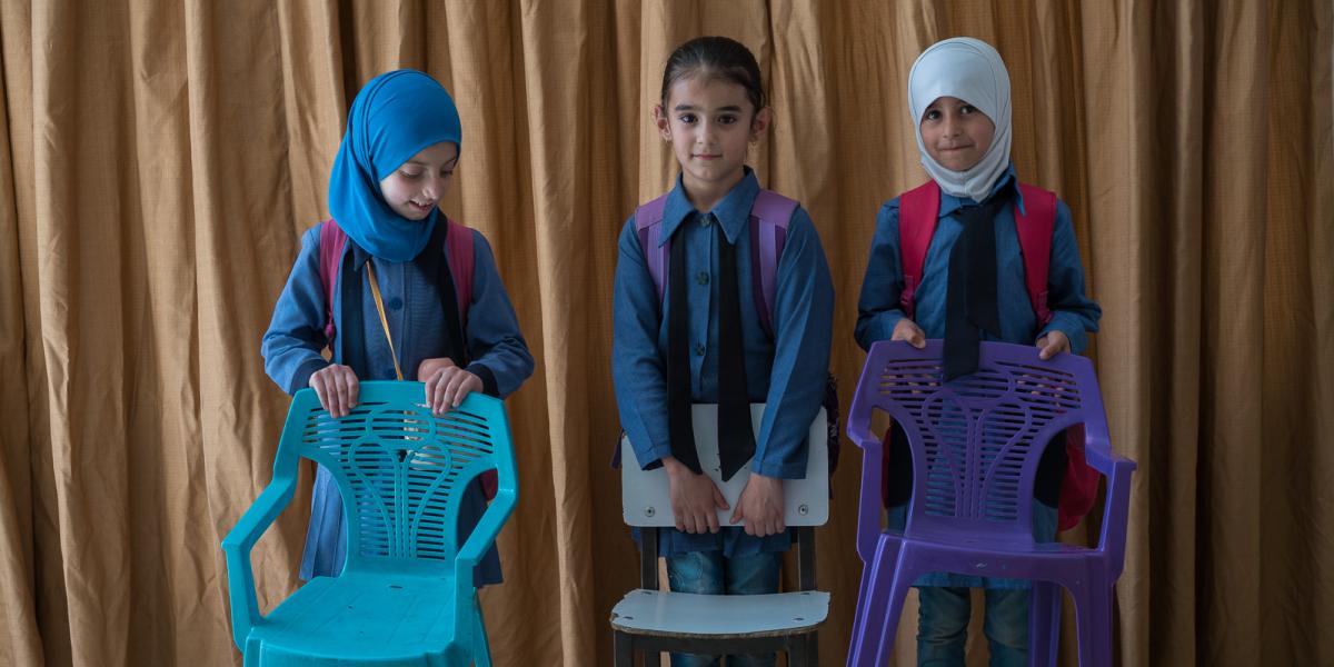Three girls holding chairs.