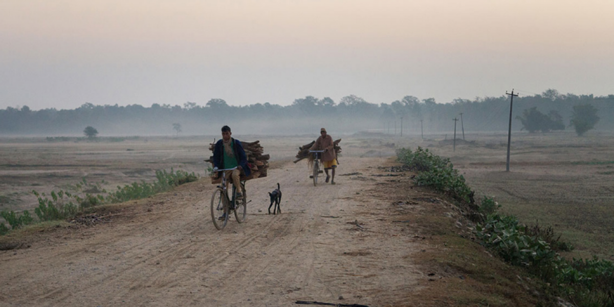 Villagers ride bikes and lead a donkey down a dirt road