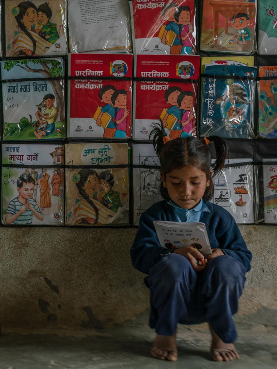 Child sitting in front of wall filled with books.