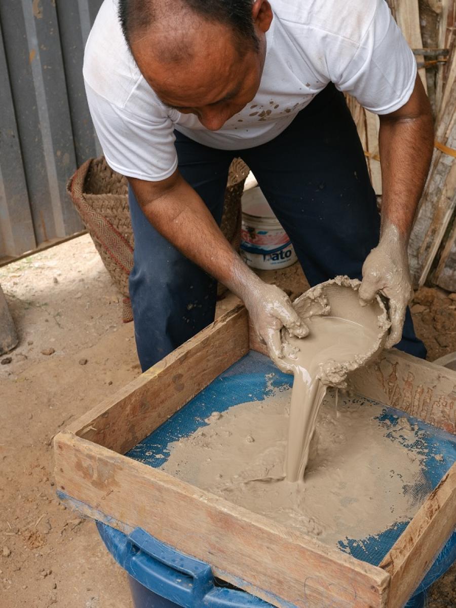 A man pours liquid clay through a strainer.