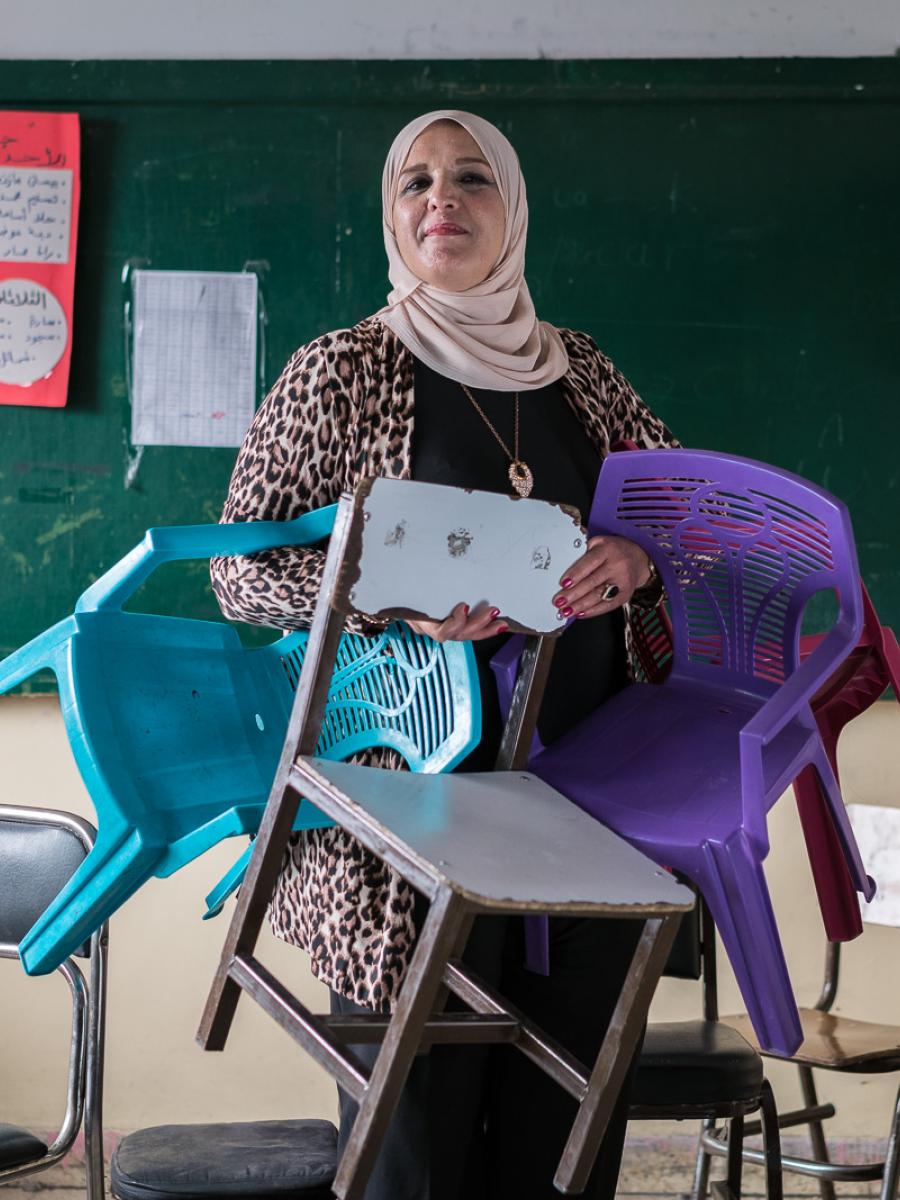 A woman holds several child-sized chairs