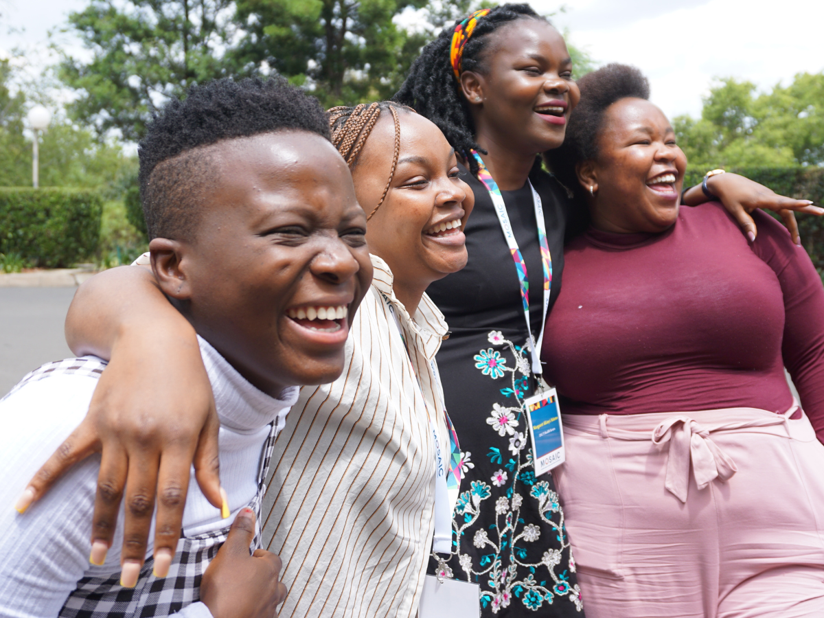 Four women are smiling posing for the camera with their arms around each other; NextGen Squad members having a laugh in Maseru, Lesotho, during MOSAIC’s HIV Prevention Ambassador Facilitators’ Training in October 2022