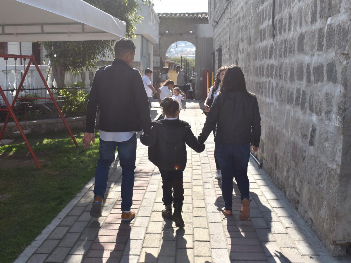 This picture shows Daniel Bracho and her family walking on a sidewalk. The picture shows their backs and other kids running around in the background.
