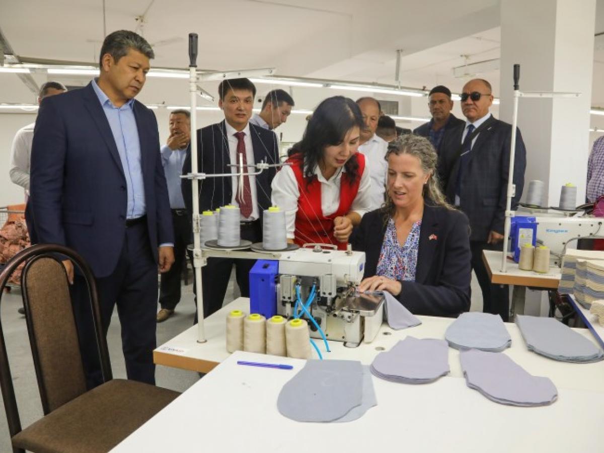 CDA Sonata Coulter sitting at a sewing machine with representatives at a garment factory
