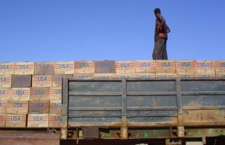 A person stands on top of a tower of emergency aid boxes. Each box is labeled "USA" . 