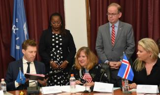 Heads of Mission from the World Bank, USAID, and Iceland sit at a table and sign a document in a conference room. 