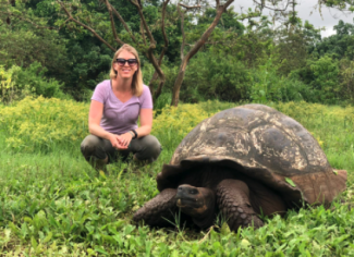 Woman crouched next to a tortoise on a field of vegetation.