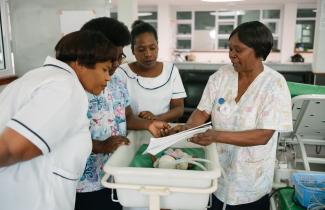 A group of women medical professionals talk around an infant crib.