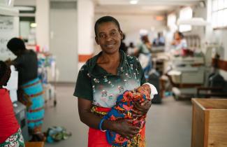 A woman holds an infant in a medical facility.