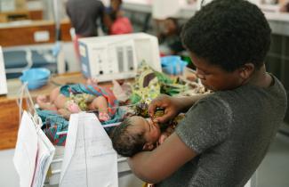 A woman holds an infant in a medical facility.