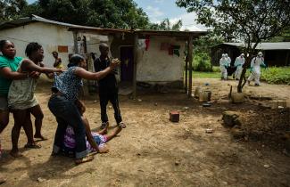 A woman cries as workers carry a deceased Ebola victim
