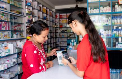 Sujata Kumari Singh, the provider and owner of a private pharmacy, requests a young client to scan the QR code to give feedback on their service.