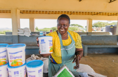 A smiling woman in Kenya stacks tubs labeled Diria.