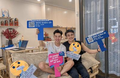 Two people hold up signs displaying information for HIV services while sitting on a couch together