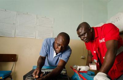 Coca-Cola Lead Cooler Technician, Maxwell Ayisi (right), and Ghana Health Services Refrigeration Technician, Livingstone Modey, repairing a dual gas/electric vaccine refrigerator at a clinic in Peki Dzake in the Volta Region of Ghana.