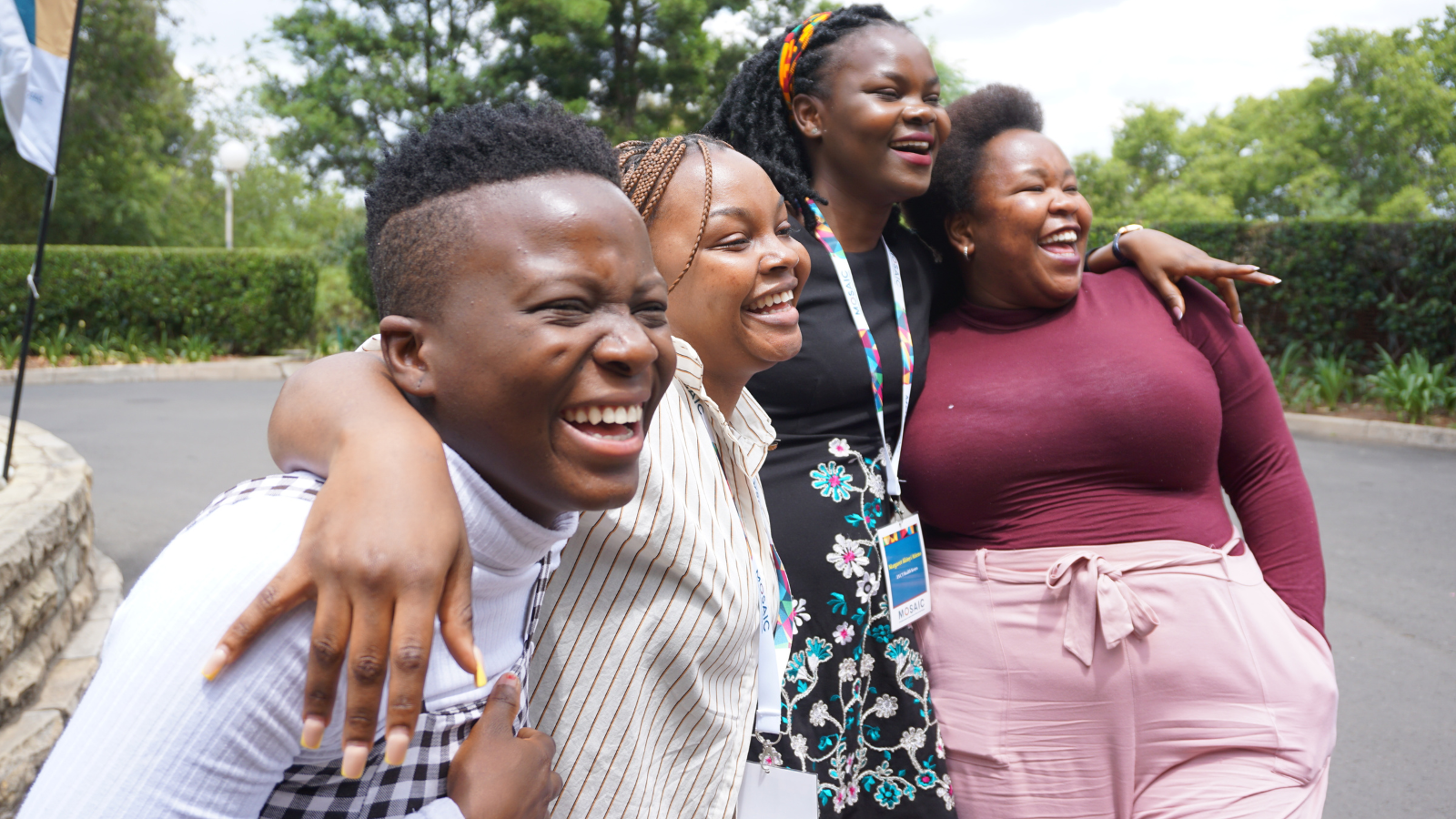 Four women are smiling posing for the camera with their arms around each other; NextGen Squad members having a laugh in Maseru, Lesotho, during MOSAIC’s HIV Prevention Ambassador Facilitators’ Training in October 2022.