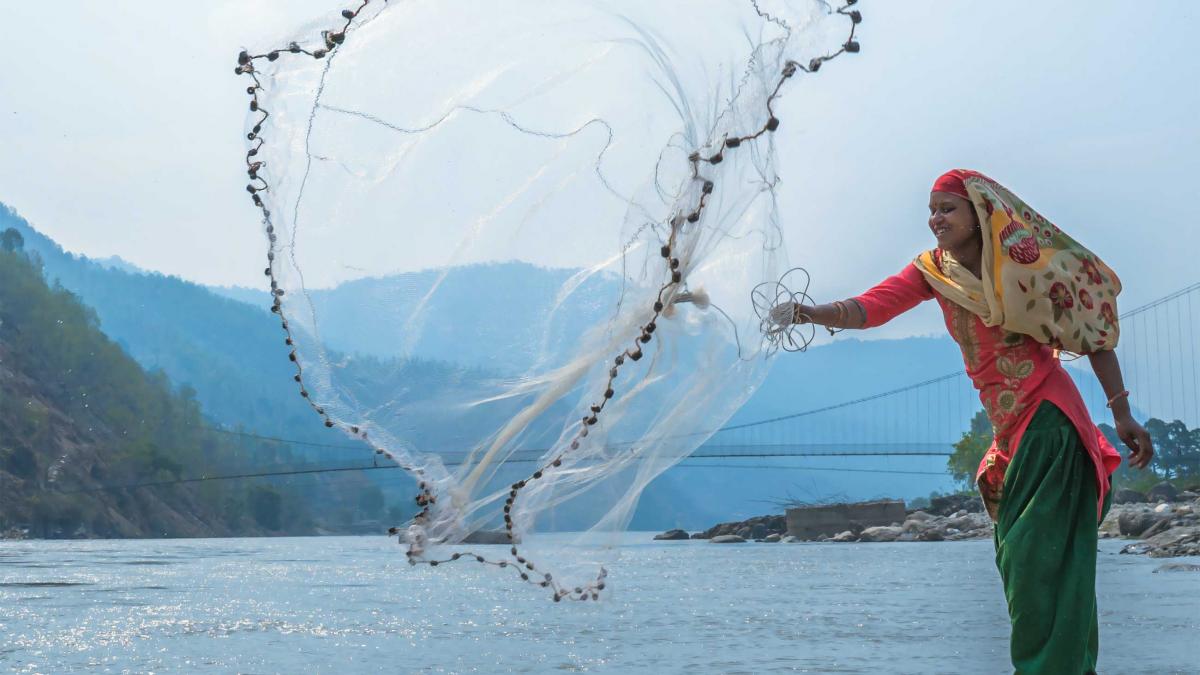 A smiling fisher woman casts her net into a river.