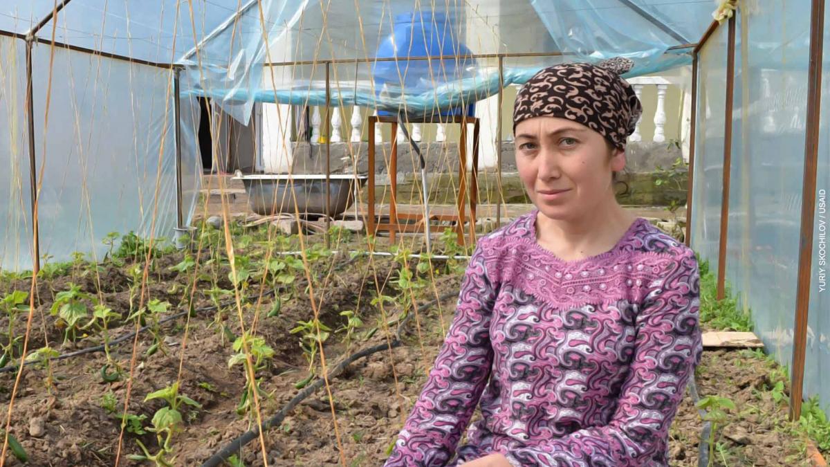 A woman sits in a greenhouse where crops are watered with highly-efficient drip irrigation.