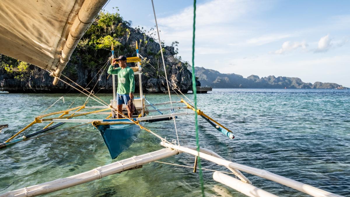 A man fishes from a boat on crystal clear water in a cove in the Philippines