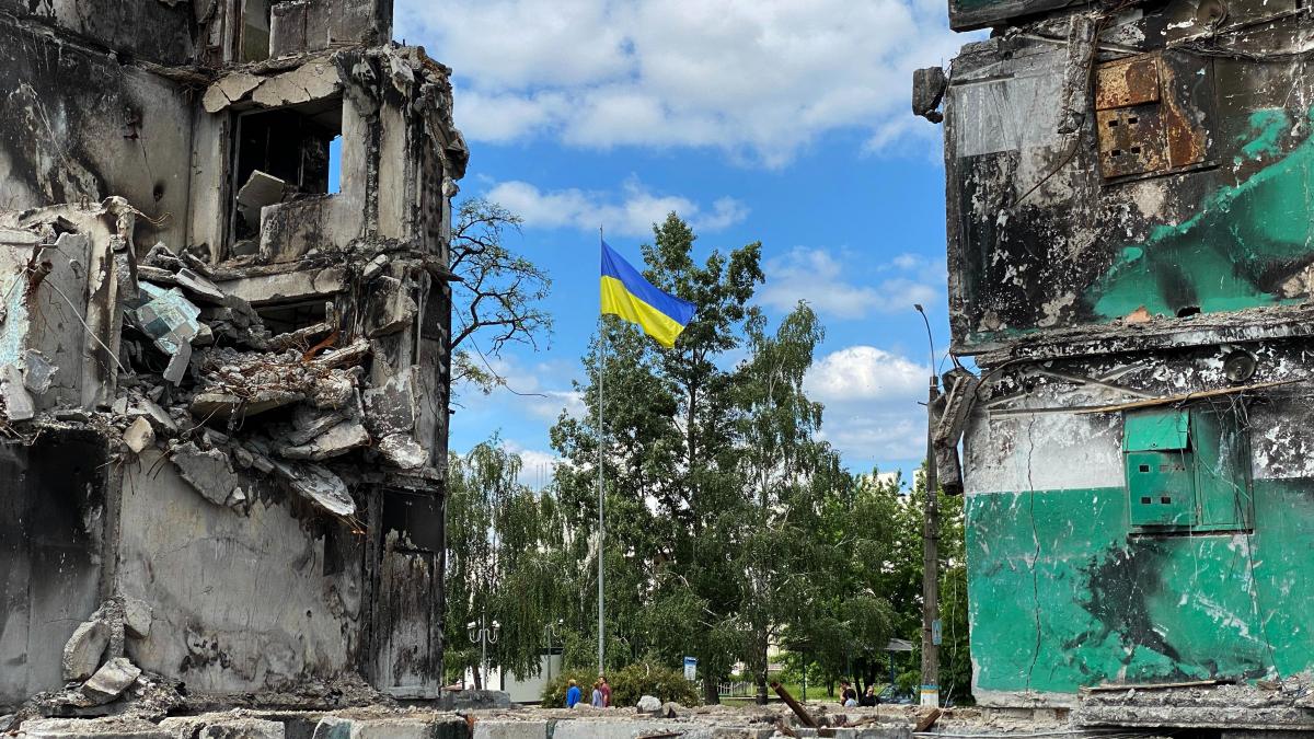 A Ukrainian flag on a pole with ruined buildings on each side. Photo by: U.S. Embassy Kyiv.