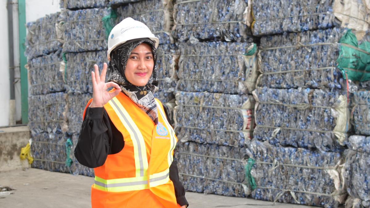 A woman is standing in front of collected plastic waste. 